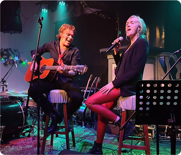 Vrolijke vrouw met blonde krullen en brede glimlach in intiem theater en concertpodium.